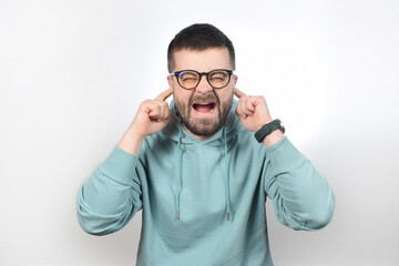 a young handsome man in glasses covers his ears with his fingers and shouts