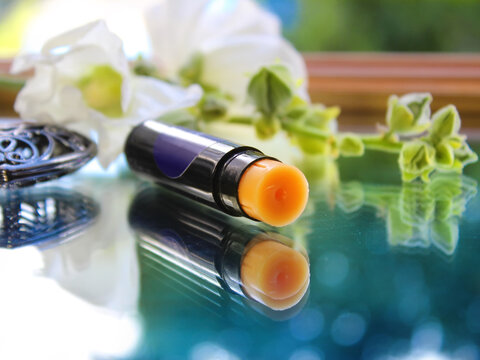 Close-up of a colorless medicated lip balm in a black tube. Reflection in the mirror. In the background is a spring mallow flower.