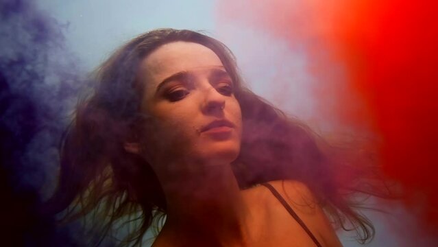 woman portrait underwater, beautiful young lady swimming in water with red and blue colored clouds