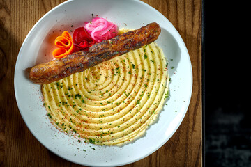 Bavarian meat sausage with a garnish of mashed potatoes, onions in a plate on a wooden background. bratwurst