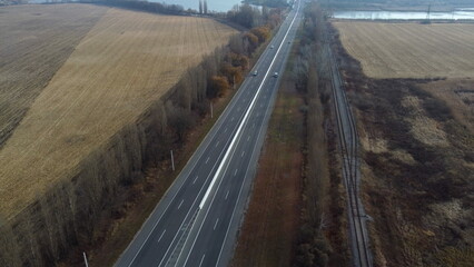 Landscape Highway, driving cars, agricultural fields after harvest, lakes on autumn day. Flying over automobile asphalt road with white markings and many cars. Perspective scenery. Aerial drone view