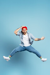 Fototapeta na wymiar Handsome excited asian man jumping high, having fun isolated on blue background. Portrait of emotional Korean dancer wearing red hat, stylish eyeglasses, white shoes. Store, shopping, sales concept
