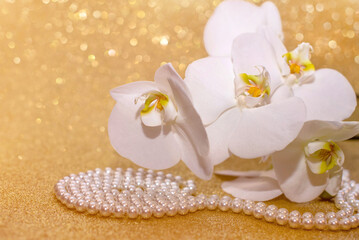 white Orchid and pearl necklace on a shiny gold background
