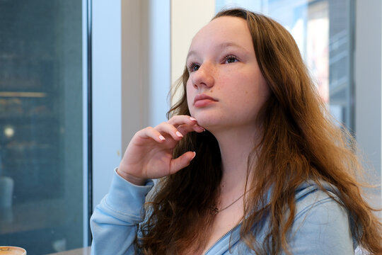 Depressed young woman near window at home, closeup. High quality photo