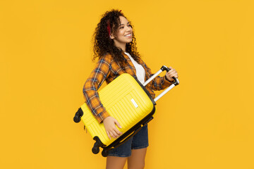 Young woman with suitcase on yellow background