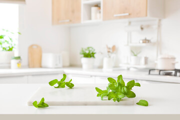 Marble cutting board with mint leaves on blurred kitchen background