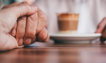 Fototapeta na wymiar Two old senior people holding hands expressing support and friendship, help and care. Elderly man and woman sitting at cafe table
