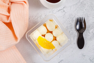 Dessert of cream, jam and orange in a plastic glass on a concrete background.