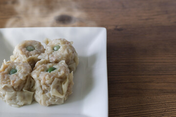 白い皿にのせ木製テーブルにおいたシュウマイ
