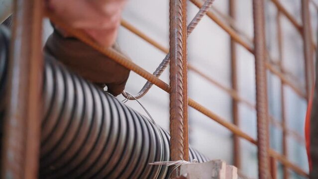 A worker tying wire to fasten piping on construction site. Slow pan right