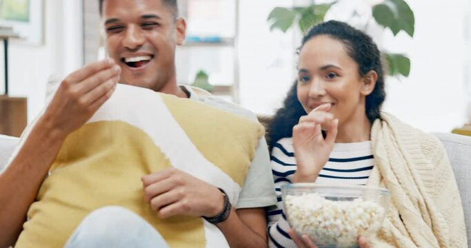 Scary movie, jump scare and young couple at home on a living room couch eating popcorn together. Fright, house and film food of a man and woman laugh with pillow, horror series and video in a lounge
