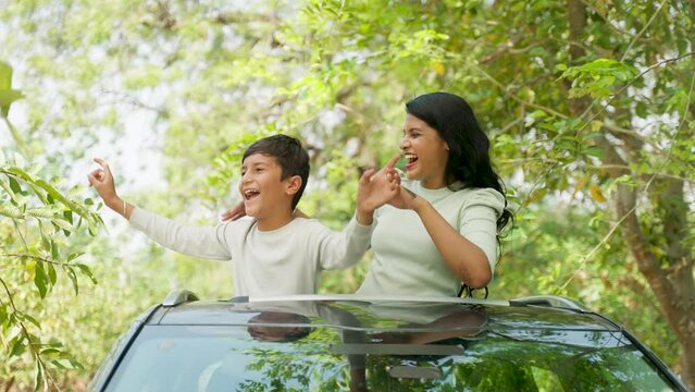 young Indian kid got excited while watching birds or animals from car sunroof while traveling in car with mother - concept of childhood freedom, summer vacation and enjoyment