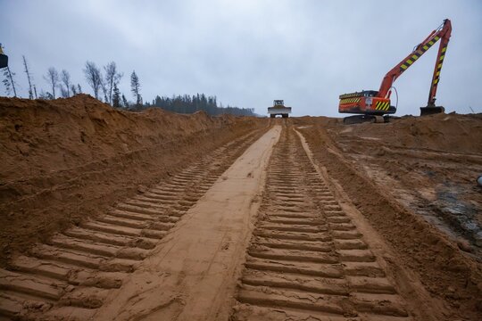 Ust-Luga, Leningrad oblast, Russia - November 16, 2021: Prints of dozer tracks on sand subbase. Road construction site. Excavator on background
