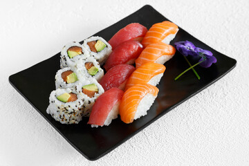 Assortiment de sushi et california rolls sur une assiette noir et fond blanc. Cuisine japonaise.