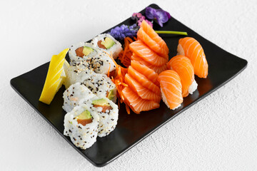Assortiment de sushi et california rolls sur une assiette noir et fond blanc. Cuisine japonaise.