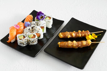Assortiment de sushi et brochettes yakitori une assiette noir et fond blanc. Cuisine japonaise.