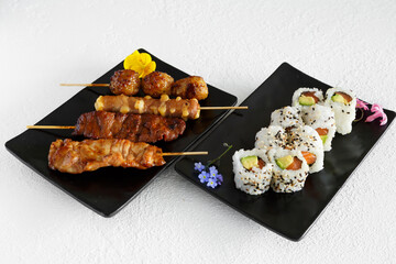 Assortiment de sushi et brochettes yakitori une assiette noir et fond blanc. Cuisine japonaise.