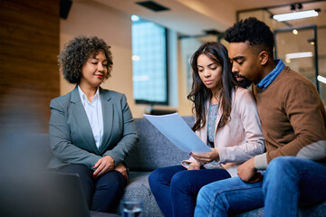 Young black couple reads financial reports while having meeting with insurance agent in office.