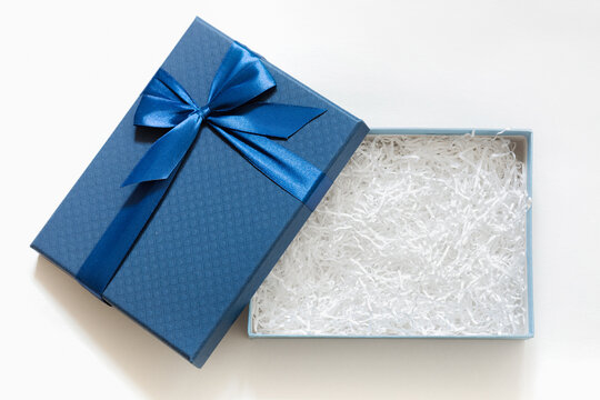 Open gift box with shredded paper on a white background. Blue cardboard box with decorative fillers for your product. Flat lay, top view, empty space for products