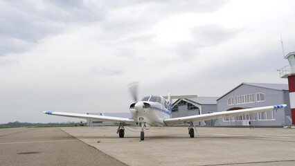 Single engine propeller airplane is standing in front of a closed aircraft hangar. Transportation for tourists and locals. Small white airplane existing hangar preparing for flight. - Powered by Adobe