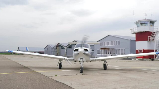 Single engine propeller airplane is standing in front of a closed aircraft hangar. Transportation for tourists and locals. Small white airplane existing hangar preparing for flight. 