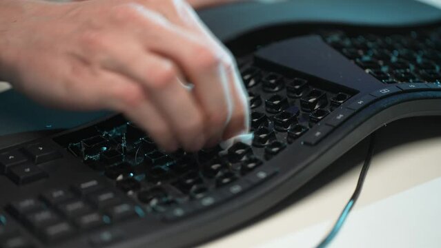 Close-up cropped shot of unrecognizable man cleaning black keyboard disassembled from buttons using wet wipes sitting at table. Concept of general cleanup on workplace. Shooting in slow motion.