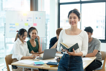 Portrait of a happy woman standing in a corporate office during a team analysis meeting. Young businesswoman discussing and analyzing a creative project in the company conference room
