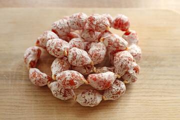 Mini salami on a wooden board. Dry-cured portioned sausage cabanossi  in a white wrapper. Sausages in a natural casing made of chicken and pork meat. Spanish sausage snacks for beer.