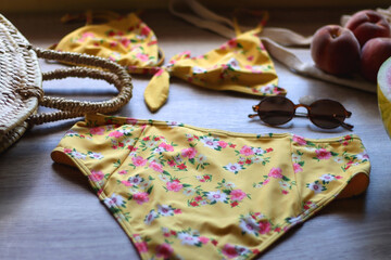 Floral yellow bikini, wicker bag, retro sunglasses, seashell, bag with peaches and cut watermelon on wooden background. Selective focus.