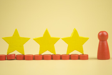 Wooden red figures peg doll standing with three yellow wooden stars. Ranking and strategy concept. Customer experience, satisfaction and best excellent services rating concept