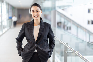 Happy young asian businesswoman smiling while walking against street blurred building background.