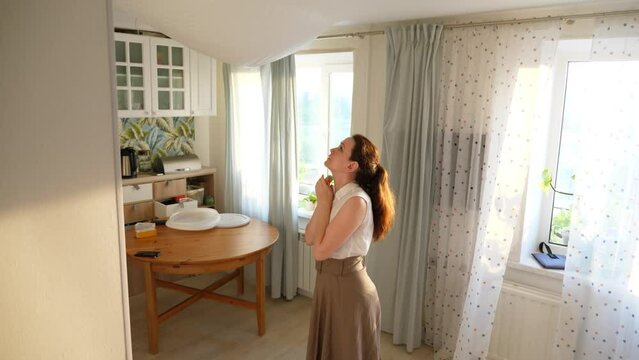 Woman worried about ceiling broken by water flood, fabric stretch and hang down in middle of living room. She get it bad, stand distressed and look up, put hands on face, touch sagging down fabric