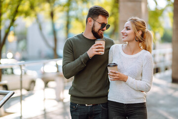 Happy young couple spending time together, drinking coffee, having fun walking around the morning city. Youth, love, time together, lifestyle.