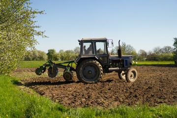 Fototapeta premium The tractor drives across the field and cultivates the land. Agricultural vehicle works in countryside. Sowing is the process of planting seeds in the ground as part of the early spring time