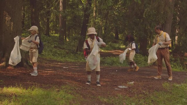 Diverse scout troop of elementary age kids and their adult leader picking up rubbish at summer forest