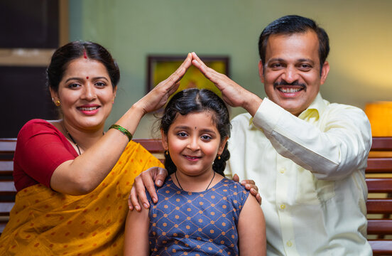 Happy Indian couple holding hands like house gesture on girl by looking at camera - concept of parental protection, empowerment and childhood support or development