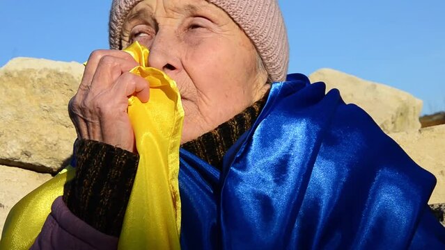 Elderly woman with Ukrainian flag. Grandmother in tears because of the war. War in Ukraine. Peace concept. Destruction of Ukrainian cities. Ukrainian refugees. Russian aggression against Ukraine.