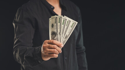Businessman holding US dollar bills while standing on a black background