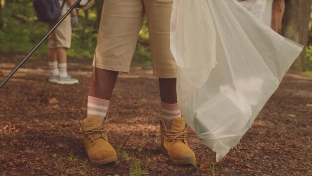 Cropped shot of unrecognizable scout collecting trash while cleaning up forest with group of other scouts and their leader in summer