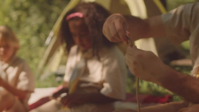 Cropped shot of unrecognizable scouter making ties while camping in forest with group of multiethnic elementary age kids