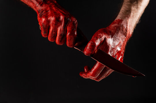 A man wipes a bloody knife with his hand on a black background. 
