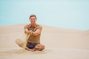 Fototapeta na wymiar Portrait of handsome middle-aged man enjoying sand of the desert and brushes it through fingers.