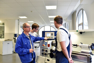 young apprentices in technical vocational training are taught by older trainers on a cnc lathes...
