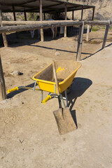 Yellow wheelbarrow of manure and a shovel in a horse stable