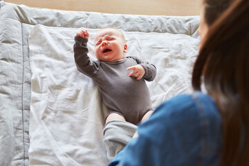 Mutter zieht schreiendem Baby Strampelanzug an