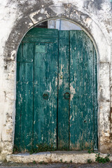 A blueish green ancient worn wooden door in a stone archway