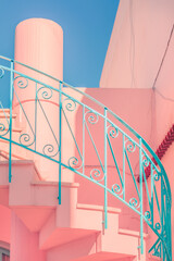 Pink colored building with a spiral staircase in the foreground and turquoise blue handrail and blue sky in the background