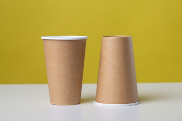 Disposable cardboard biodegradable glass on a white table, yellow background.