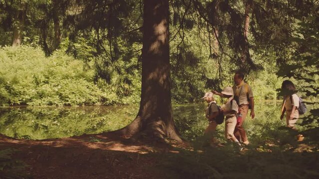 Full length shot of multiethnic scout troop with adult leader in head hiking along forest trails on sunny day