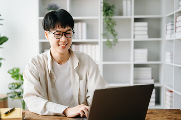 Fototapeta premium Handsome and talented young Asian man student working on his project assignment, using laptop and tablet to search an online informations..